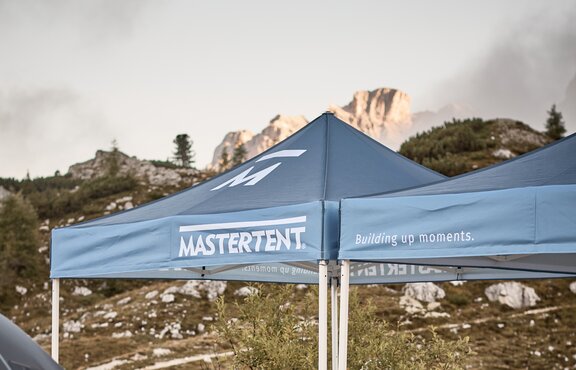 Blue printed canopy tents with Mastertent logos set up with mountains in the background.