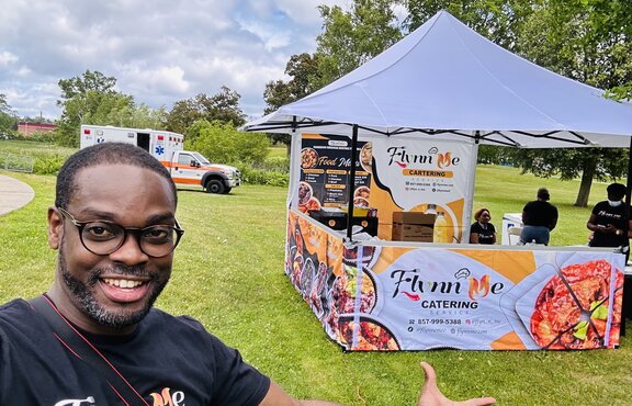 A man standing in front of his Mastertent printed vending canopy tent with awning on a grass field.