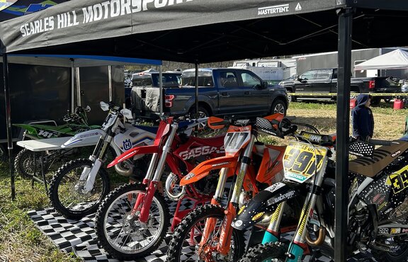 A 15x10 custom motorsports tent with a black roof covers dirt bikes prior to a race. 