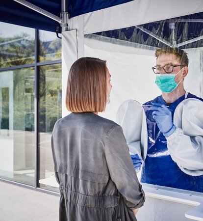 L'impiegato all'interno della tenda esegue un test di striscio sulla donna che si trova davanti. Indossa un paradenti e dei guanti.