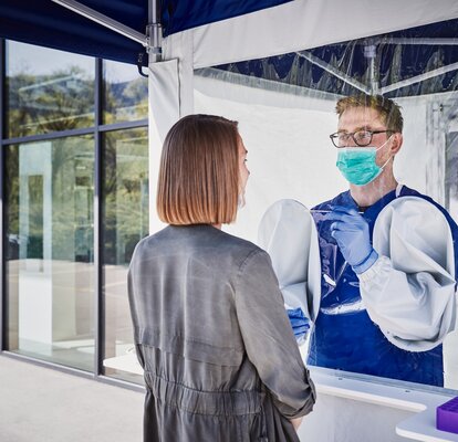 L'impiegato all'interno della tenda esegue un test di striscio sulla donna che si trova davanti. Indossa un paradenti e dei guanti.