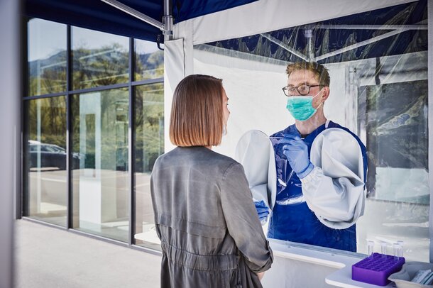 L'impiegato all'interno della tenda esegue un test di striscio sulla donna che si trova davanti. Indossa un paradenti e dei guanti.