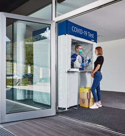 Corona test cabin at the entrance. The woman is standing in front of it and getting herself tested.