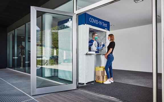 Corona test cabin at the entrance. The woman is standing in front of it and getting herself tested.