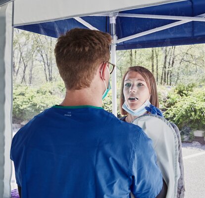 Il dipendente all'interno del gazebo esegue un test di striscio attraverso i guanti integrati nel gazebo. La donna è di fronte alla cabina di prova.