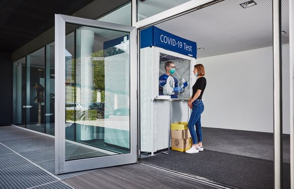 Corona-Testkabine am Eingang. Die Frau steht davor und lässt sich testen.