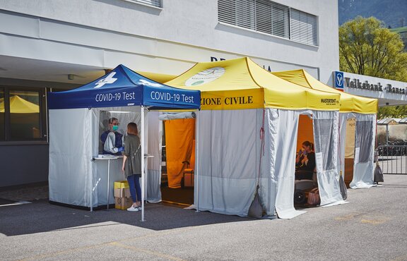 Die Testkabine für Covid-19 und zum Fiebermessen steht vor der Privatklinik Brixana. Daneben stehen noch zwei Faltpavillons mit gelben Dächern.