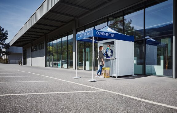 Die Frau befindet sich vor der Covid-19 Testkabine. An ihr wird Fieber gemessen oder ein Abstrich genommen.