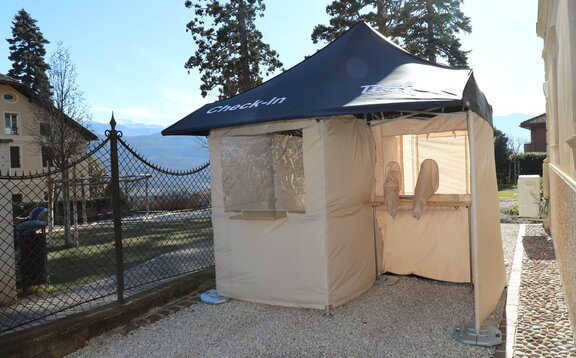 The Covid-19 series test station is in front of the Kaltern pharmacy in Goldgasse. The roof is blue, the side walls grey and the sun is shining in the sky.