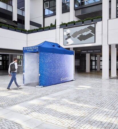 C'è un tunnel di disinfezione blu di fronte ad un edificio. La persona sta per attraversarlo in modo da essere disinfettata dalla testa ai piedi e quindi protetta.