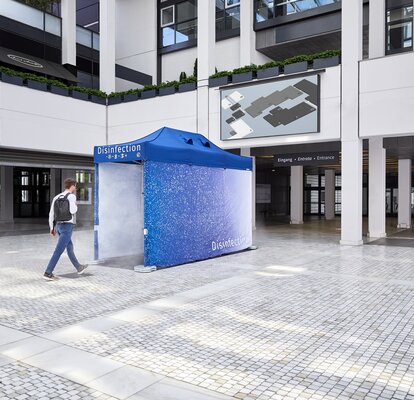 There is a blue disinfection tunnel in front of a building. The person is just about to walk through it so that he is disinfected from head to toe and thus protected.