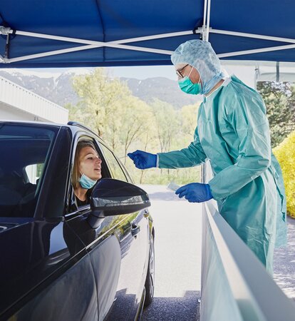 At the drive-in test station, the hospital employee is taking a smear test on the woman in the car.