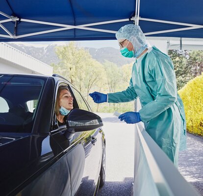 At the drive-in test station, the hospital employee is taking a smear test on the woman in the car.