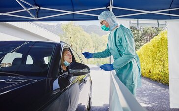 Der Mitarbeiter vom Krankenhaus macht in der Drive-In Teststation gerade einen Abstrich bei der Frau im Auto.