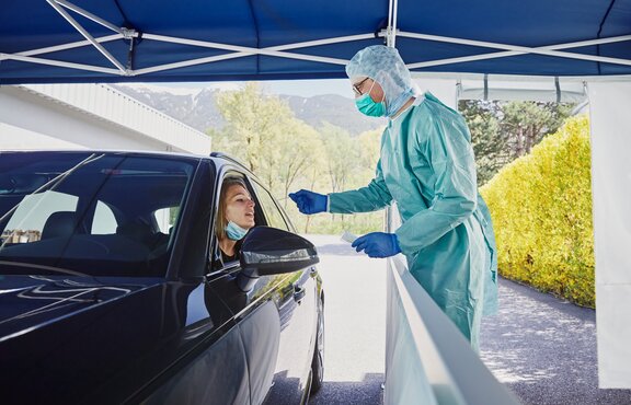 Der Mitarbeiter vom Krankenhaus macht in der Drive-In Teststation gerade einen Abstrich bei der Frau im Auto.