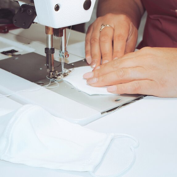 Woman sewing white cloth mask.