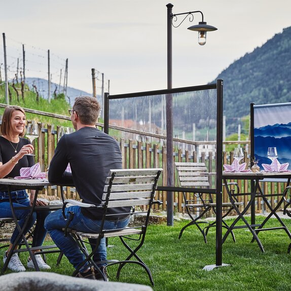 Dividing wall stands between the tables in the guest garden. The couple is sitting at a set table. Behind it you can see a printed partition wall.