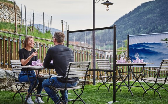 Dividing wall stands between the tables in the guest garden. The couple is sitting at a set table. Behind it you can see a printed partition wall.