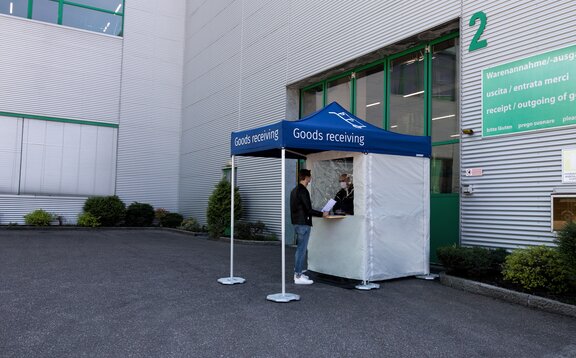 The man is standing in front of the goods receiving station. The employee is in the gazebo.