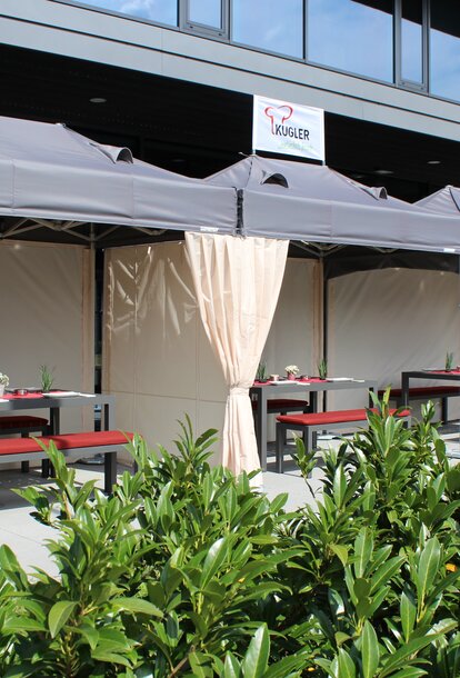 The terrace in front of the restaurant is covered with three folding tents. Below them are set tables for the guests.