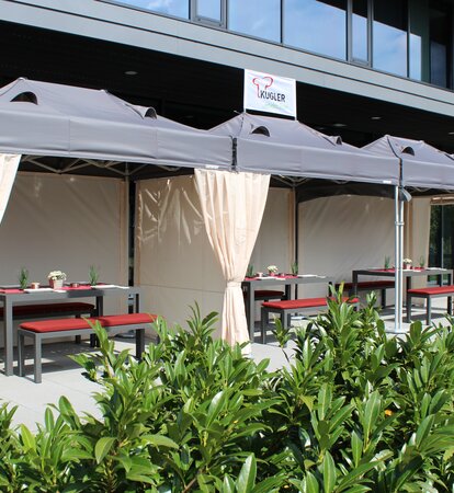 The terrace in front of the restaurant is covered with three folding tents. Below them are set tables for the guests.