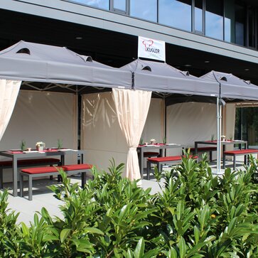 Die Terrasse vor dem Restaurant ist mit drei Faltzelten überdacht. Darunter befinden sich gedeckte Tische für die Gäste.