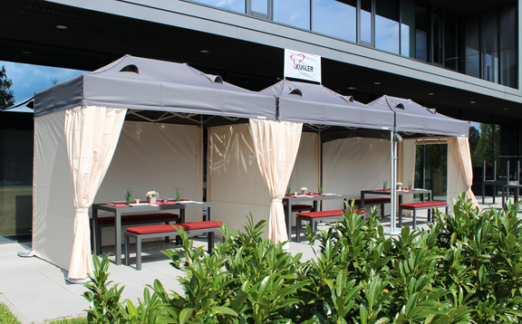 Die Terrasse vor dem Restaurant ist mit drei Faltzelten überdacht. Darunter befinden sich gedeckte Tische für die Gäste.