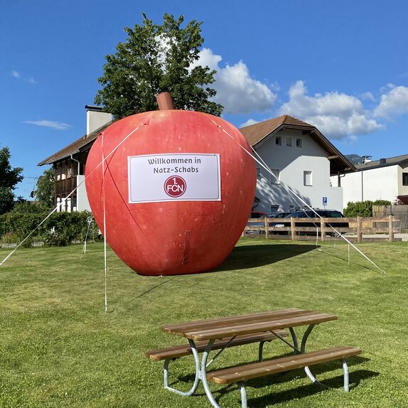 Auf einer Wiese steht ein großer, roter Apfel. Es ist ein aufblasbarer Werbeträger.