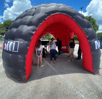 Su una piazza c'è un gonfiabile pubblicitario di Mobil 1 in rosso e nero. Sotto di esso ci sono alcune persone.