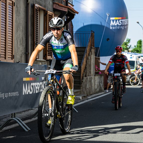 The picture shows two cyclists and in the background a large, blue and roundish Mastertent advertising medium.