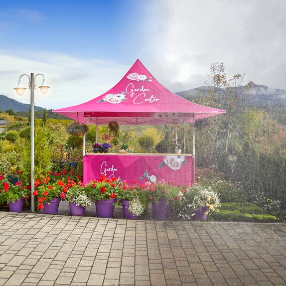 Ein pinker wasserdichter Faltpavillon von Mastertent befindet sich halb im Regen und halb im Sonnenschein. Davor stehen Blumen. 