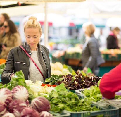 Marktstand am Bauernmarkt Eine Frau steht vor einem Marktstand und sucht sich Gemüse aus.