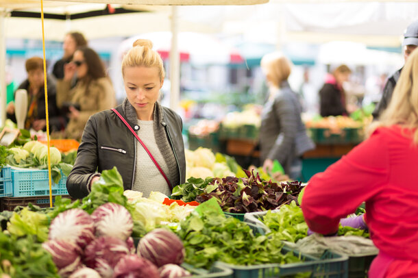 Eine Frau steht vor einem Marktstand und sucht sich Gemüse aus. 