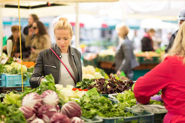 Eine Frau steht vor einem Marktstand und sucht sich Gemüse aus. 