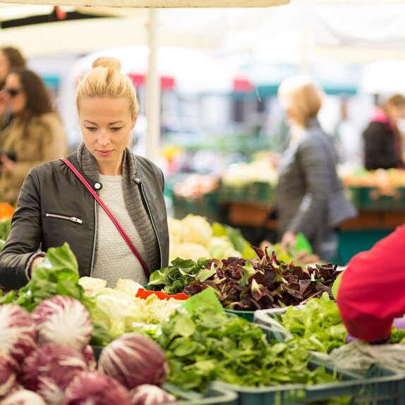 Eine Frau steht vor einem Marktstand und sucht sich Gemüse aus. 