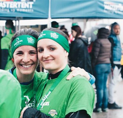 2 Läuferinnen lachen zufrieden nach einem Marathon. Mastertents Faltzelte stehen im Hintergrund.. 