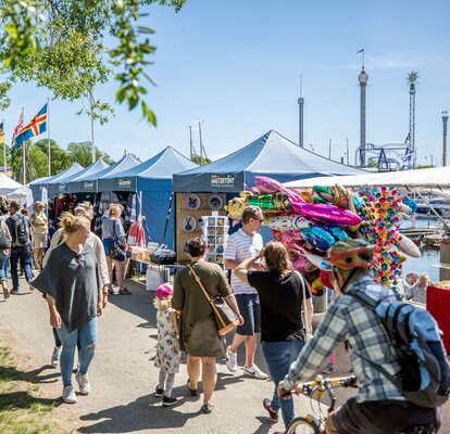 Mastertent's gazebos are used as market tents. It is a beautiful summer day. People laugh. 