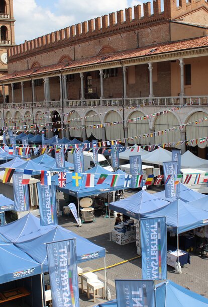 Three blue gazebos in a row are standing on a town square. The flags of different nations are 