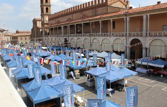 Gazebo pieghevoli blu in piazza. Sopra i gazebo pieghevoli ci sono delle bandiere di nazioni diverse. 