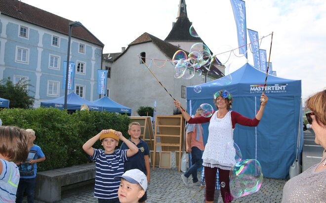 Eine Straßenkünstlerin unterhält die Kinder, indem Sie große Seifenblasen formt.