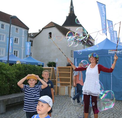 Eine Straßenkünstlerin unterhält die Kinder, indem Sie große Seifenblasen formt.