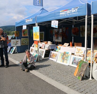 Straßenkünstler stehen und sitzen vor einem blauen MASTERTENT Faltpavillon und stellen Ihre Kunstwerke vor.