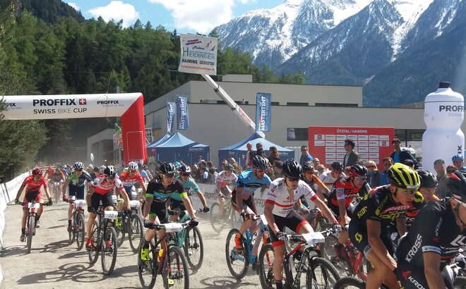 Teinehmer des PROFFIX Swiss Bike Cup fahren eng nebeneinander und kämpfen um den Sieg. Im Hintergrund stehen blaue MASTERTENT Faltpavillons.