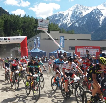 Teinehmer des PROFFIX Swiss Bike Cup fahren eng nebeneinander und kämpfen um den Sieg. Im Hintergrund stehen blaue MASTERTENT Faltpavillons.