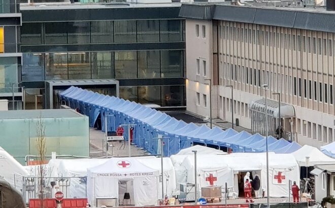Blaue Faltpavillons von Mastertent bilden einen langen Korridor vor dem Krankenhaus Bozen zur Bekämpfung des Coronavirus. Davor sieht man noch einige Zelte des roten Kreuz.