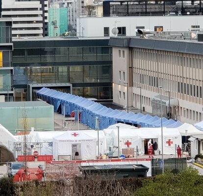 Blaue Faltpavillons von Mastertent bilden einen langen Korridor vor dem Krankenhaus Bozen zur Bekämpfung des Coronavirus. Davor sieht man noch einige Zelte des roten Kreuz.