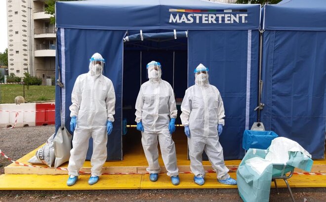 3 Sanitäter in Schutzanzügen stehen vor einem blauen Faltzelt von Mastertent. 