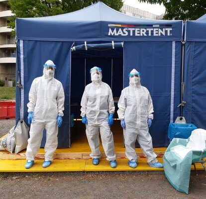 Corona Test-Kabine von Mastertent 3 Sanitäter in Schutzanzügen stehen vor einem blauen Faltzelt von Mastertent.