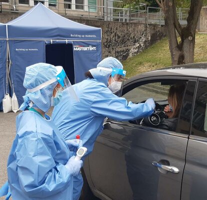 Zwei Sanitäterinnen nehmen von einer Autofahrerin Testabstriche. Dahinter steht ein blaues Mastertent Faltzelt. 