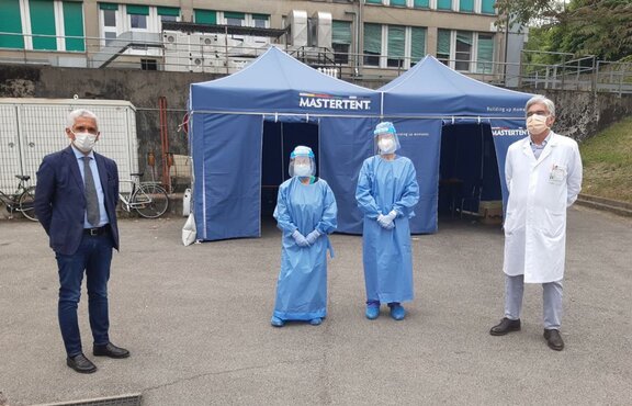 2 paramedics, 1 doctor and a coordinator stand in front of a blue Mastertent folding tent. 